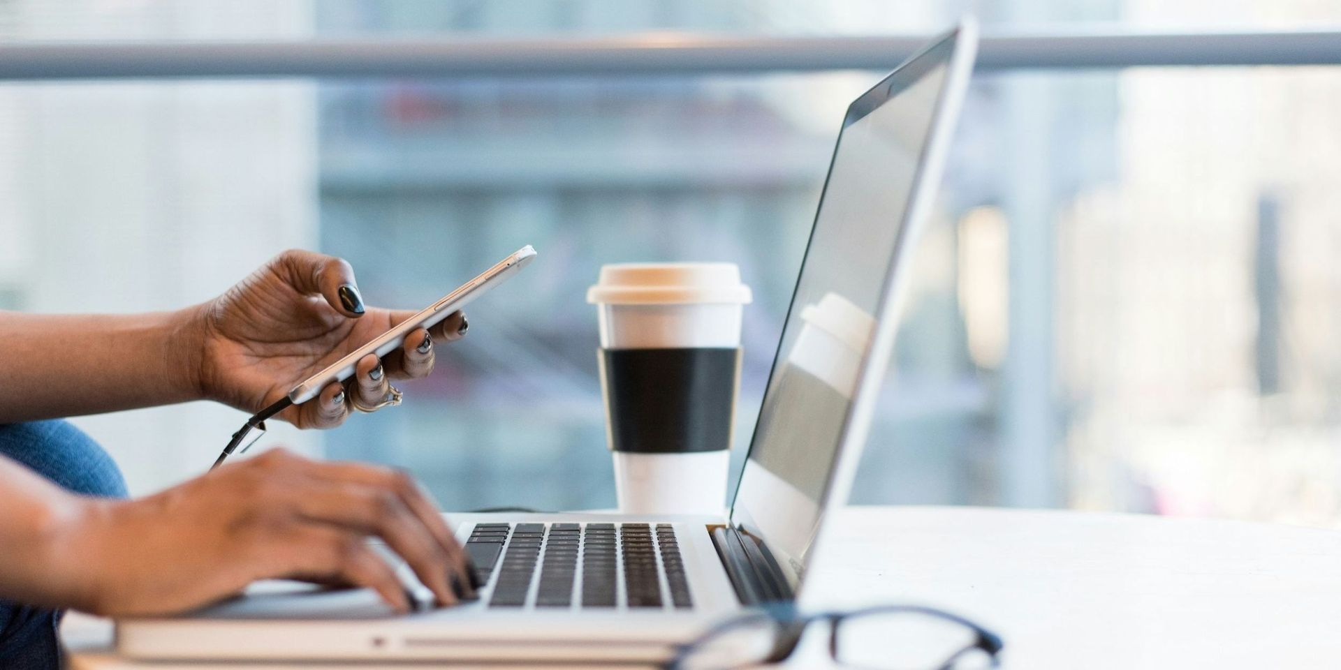 close up of person's hands typing on laptop and holding mobile phone